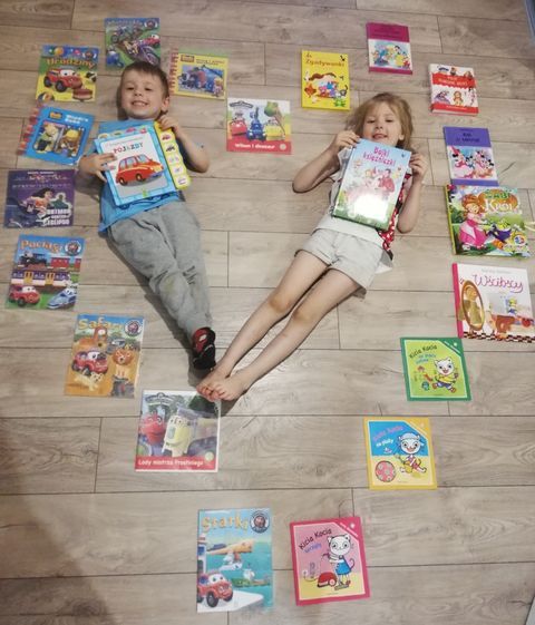 Dziewczynka i chłopiec leżą na podłodze tworząc serce. Wokół nich ułożone w serce książki