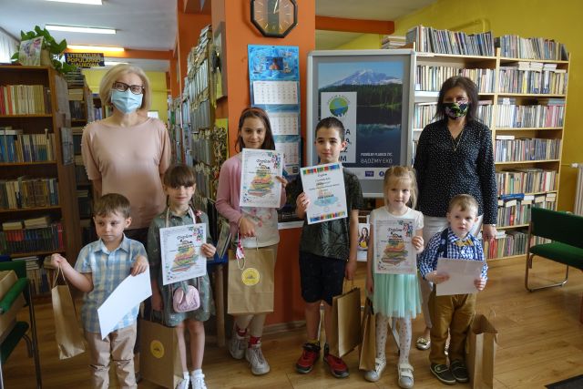 Na pierwszym planie Najaktywniejsi Czytelnicy roku 2020, w tle regały biblioteczne