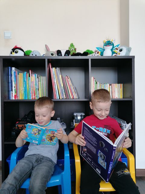 Dwóch chłopców czytających książki, w tle regał z książkami