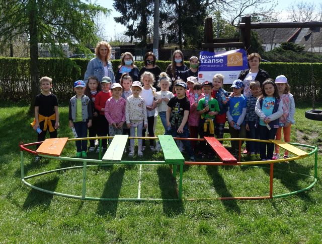 11 dzieci stoi, za nimi dyrektorka biblioteki i bibliotekarka, 2 uczennice szkoły podstawowej oraz wychowawczyni grupy