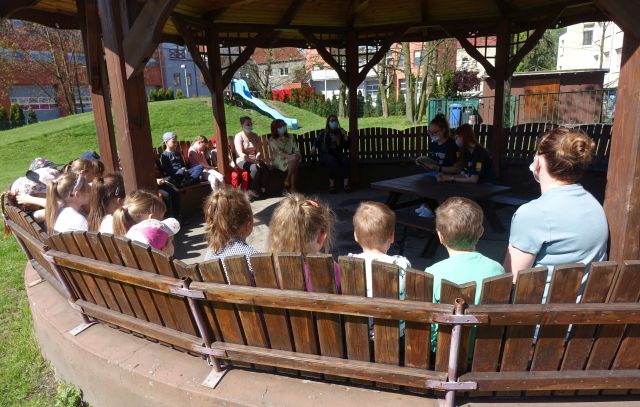 Na zdjęciu dzieci, siedzące na ławkach z grupy Stokrotki z Przedszkola Miś, dyrektorka biblioteki i bibliotekarka, 2 uczennice szkoły podstawowej oraz dyrektorka przedszkola