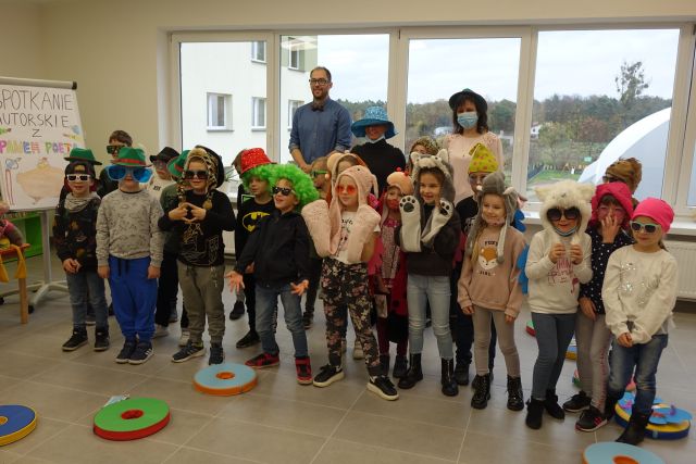 w tle mężczyzna, obok kobieta w kapeluszu czarnym, przed nimi stojące przebrane dzieci