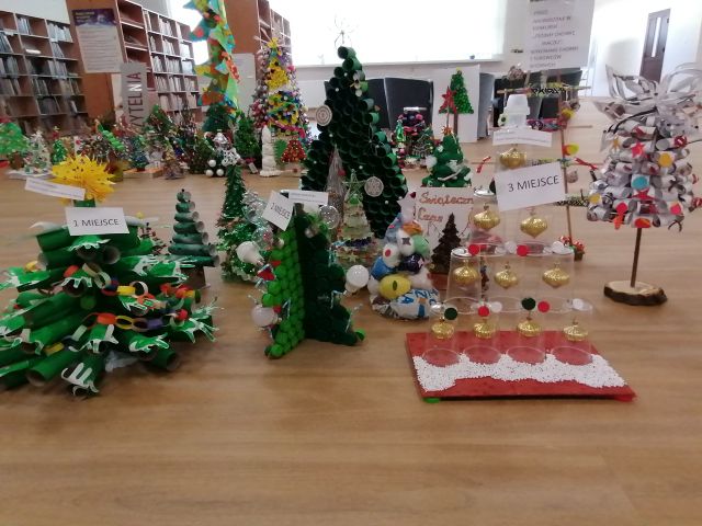 na brązowej podłodze 16 kolorowych choinek wykonanych z surowców wtórnych