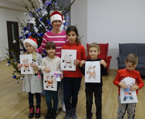 5 dzieci i bibliotekarka stoją przed choinką, w dłoniach trzymają wykonane przez siebie rysunki z mikołajem