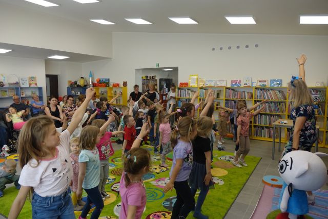 na zielonym dywanie stoją dzieci z wyciągniętymi w górę rękoma, udają lecący samolot