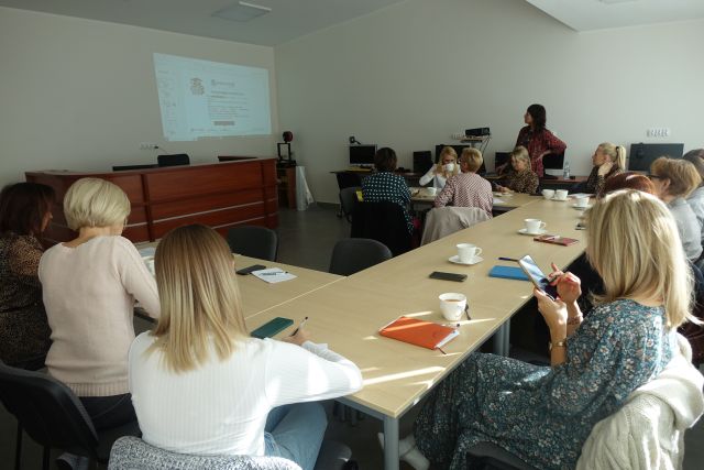 uczestnicy szkolenia siedzą przy brązowych stołach, w tle prezentacja wyświetlana na ścianie