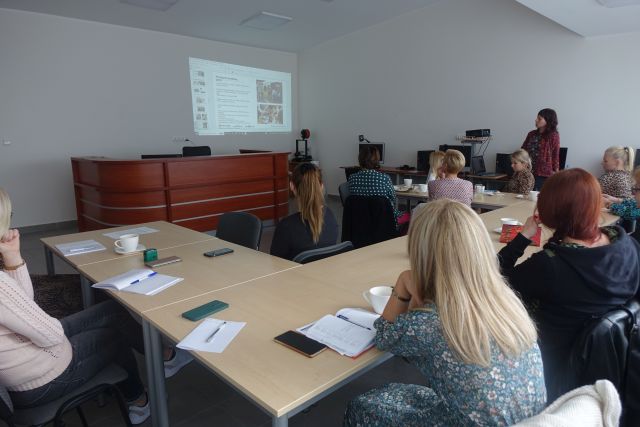 uczestnicy szkolenia siedzą przy stołąch, przed nimi na ścienie wyświetlana prezentacja