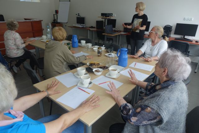 przy brązowych stołach siedzą starsze kobiety, przed sobą mają kartki papieru