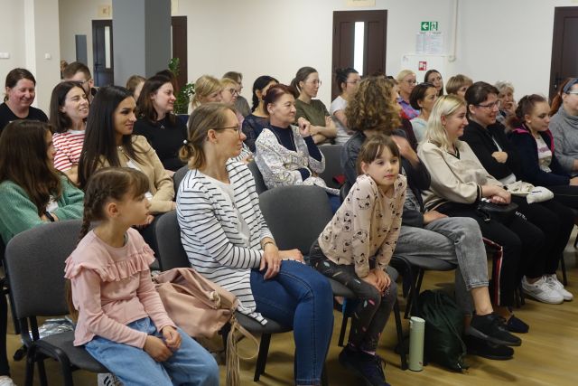na siwych krzesłach siedzą osoby uczestniczące w spotkaniu