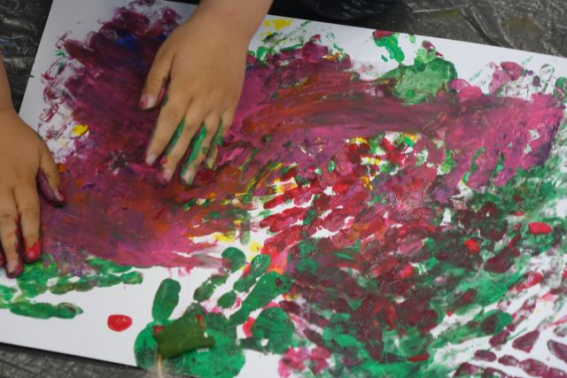 kartka wypaćkana różnymi kolorami i dłoń dziecka ubrudzona zieloną farbą
