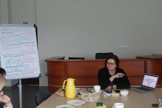 przy stołach siedzą uczestnicy szkolenia, w tle brązowe biurko