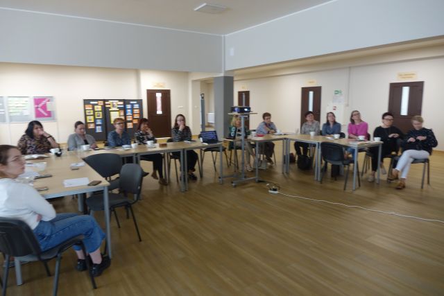 w hoolu biblioteki przy brązowych stołach siedzą kobiety, na stołach mają filiżanki i zeszyty