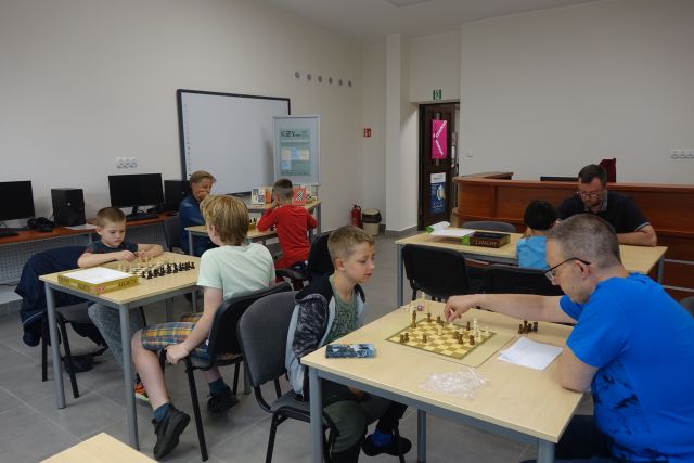 przy brązowych stołach siedzą mali szachiści i grają w szachy