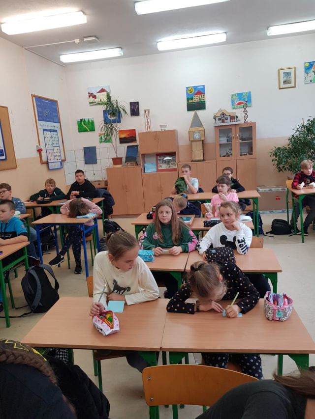 dzieci siedzą przy brązowych ławka w sali klasowej i spisują na karteczkach jaka jest ich biblioteka marzeń, w tle szafa