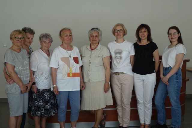 8 kobiet stoi, za nimi w tle ekran i brązowe biurko