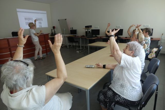 przy brązowych stołach siedzą kobiety z unisionymyi dłońmi