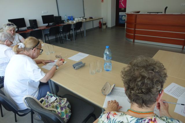 przy brązowych stołach siedzą kobiety i piszą na kartkach