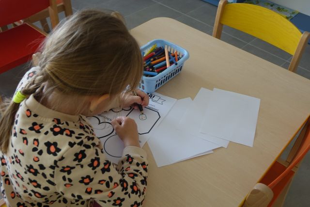 przy brązowym stole siedzi dziewczynka i rysuje na białej kartce