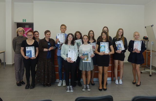 w dwóch rzędach stoją dziewczyny i chłopcy oraz dwie kobiety. Młodzież trzyma w rękach dyplomy i książki