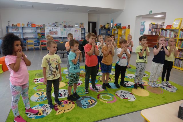 na zielonym dywanie stoją dzieci, za nimi w tle widać niebieskie regały