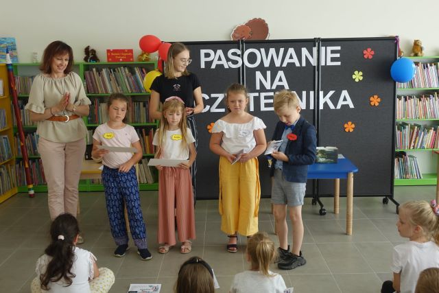 dzieci stoją i trzymają w dłoniach nagrody, za nimi stoją dwie kobiety, za nimi czarna tablica