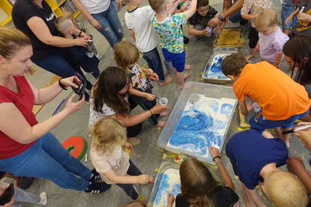 dzieci i opikunowie siedzą przed tackami z mlekiem i barwnikami