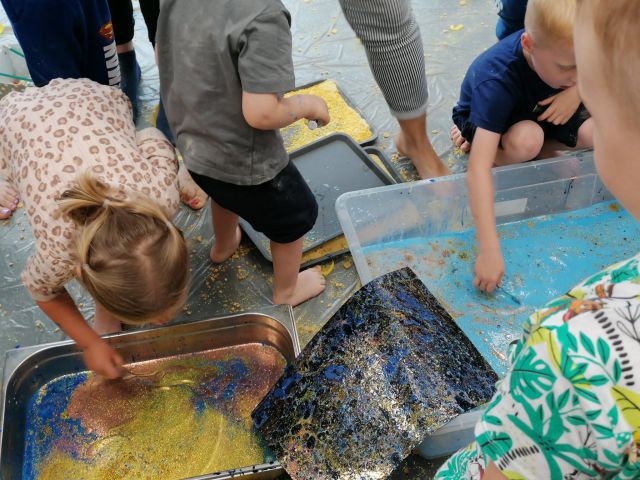 dzieci maczają w tackach z mlekiem i farbkami papier
