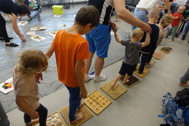 po drewnianych ramkach z różnymi materiałami idą dzieci