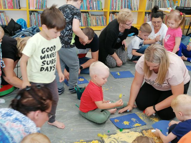 dzieci i rodzice siedzą na podłodze i kleją na niebieskim papierze niebo