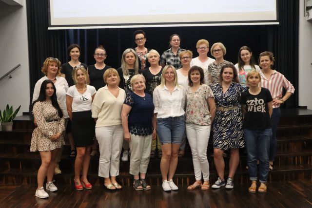 w trzech rzędach na schodach stoją kobiety, za nimi biały ekran