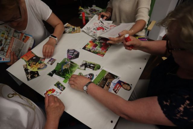 na stole duży arkusz papieru wyklejony zdjęciami z gazet, w koło widać dłonie