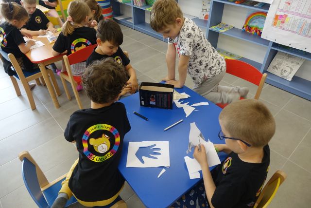 przy niebieskim stole siedzą dzieci i wycinają z kartek ręce