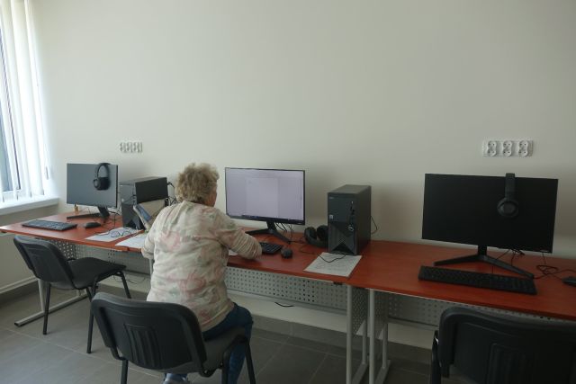 przy brązowym biurku tyłem siedzi kobieta przed komputerem