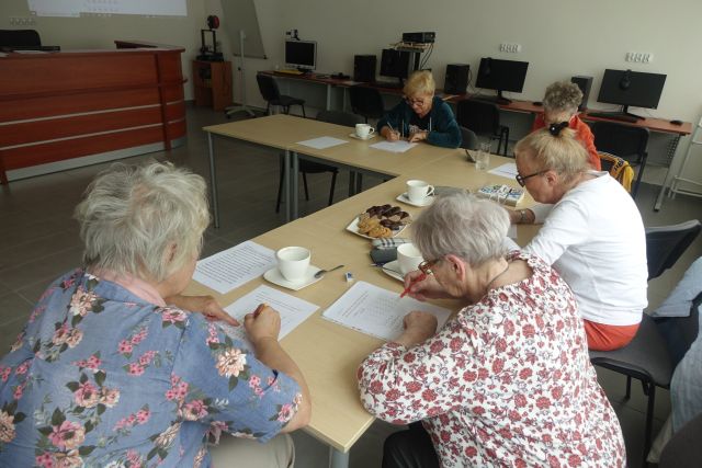 przy brązowych stołąch siedzi 5 kobiet i piszą na kartkach