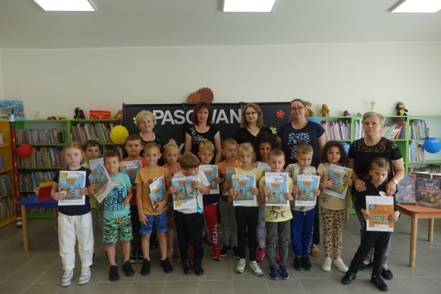 dzieci stoją w dwóch rzędach i trzymają w dłoniach dyplomy i książki, za nimi stoją 4 kobiety, za nimi czarna tablica