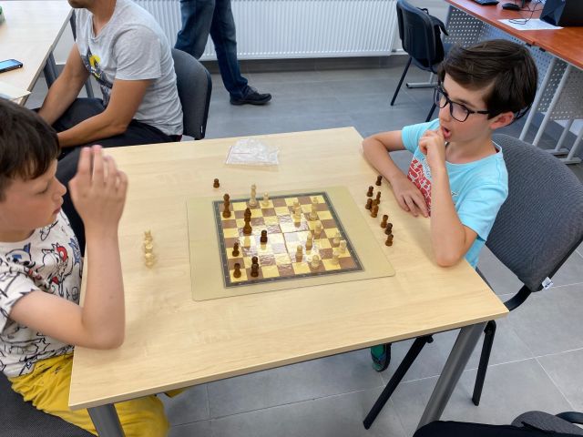 przy brązowym stole siedzi dwóch młodych szachistów, na stole szachy