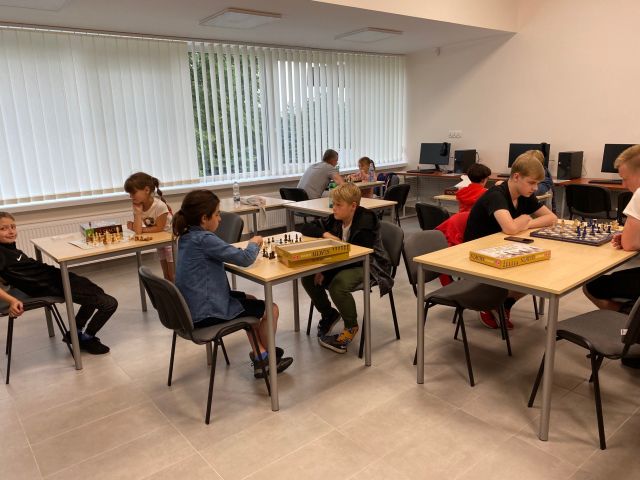 przy brązowych stołach siedzi młodzież i gra w szachy