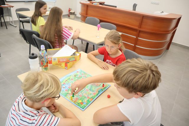 przy brązowych stołach dzieci grają w gry planszowe