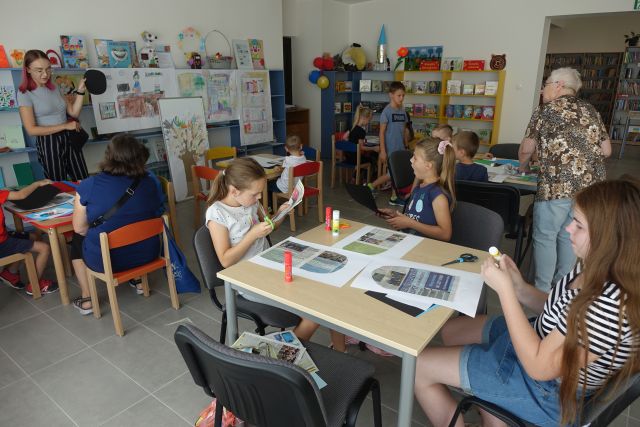 przy brązowych stołach siedzą dzieci i wycinają z gazet