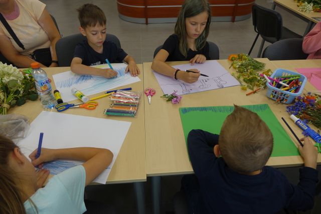 przy brązowych stołach siedzą dzieci i wyklejają na kartkach marzenia z kwiatów