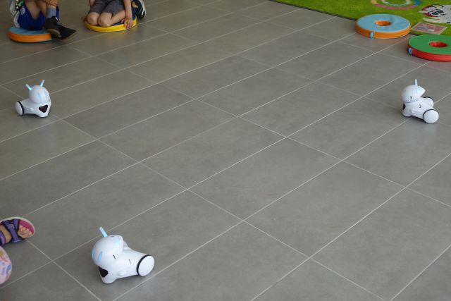 po siwej podłodze jeżdżą trzy małe białe roboty