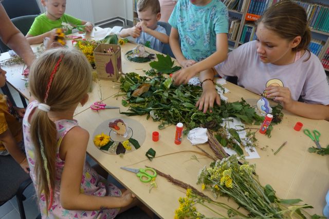 przy brązowych stołach pracują dzieci - wyklejają gniazda dla ptaków z roślin i kwiatów