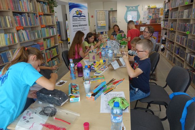 przy brązowych stołach siedzą dzieci i kleją i malują zwierzątka z tektury