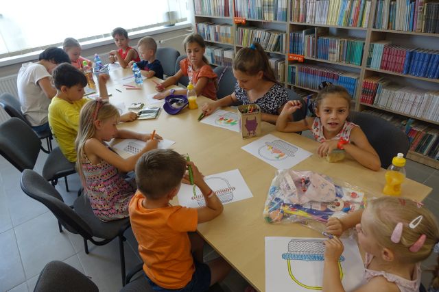 przy brązowych stołach siedzą dzieci i malują koszyczki