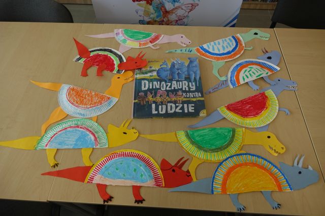 na brązowym stole leżą wykonane przez dzieci z papierowych talerzyków dinozaury