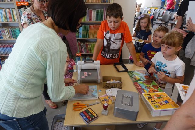 przy stole stoi kobieta i robi puzle, stoją dzieci