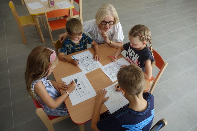 przy brązowycm stole siedzą dzieci i rozwiązują zagadki