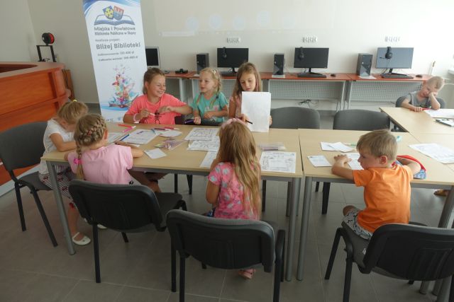 dzieci siedzą przy stołach i rozwiązują zagadki