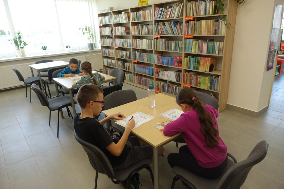 dzieci siedzą przy brązowych stołacch i rozwiązują zadania
