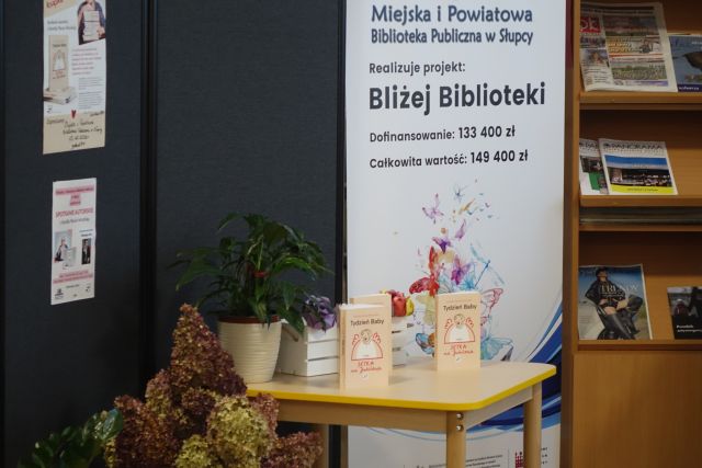 na stoliku książki, za stolikiem plakat z nazwą projektu